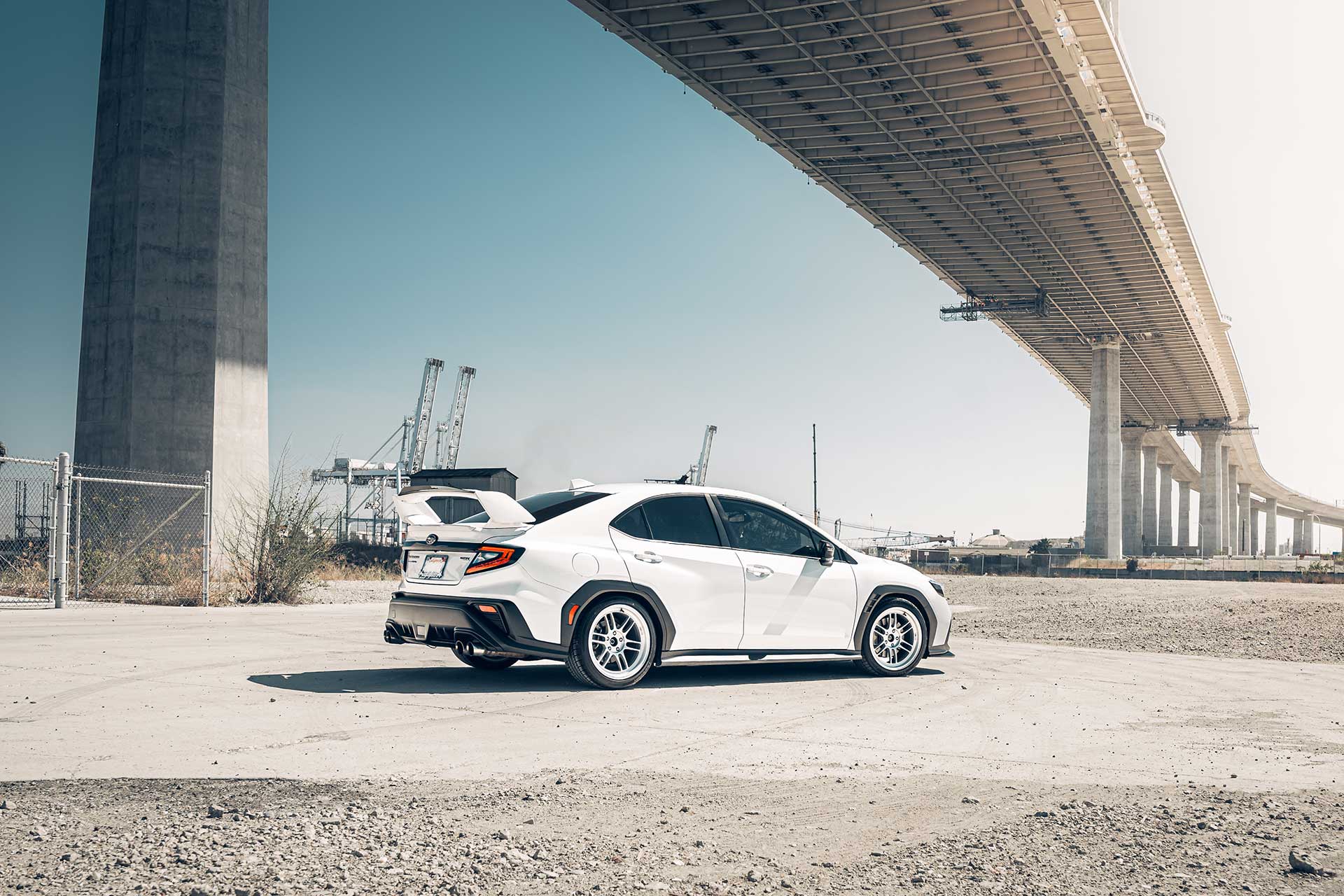 white subaru wrx with lionhart ramani all season tires parked under concrete bridge with industrial port cranes in background
